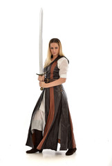 full length portrait of girl wearing brown  fantasy costume, holding a sword. standing pose on white studio background. 