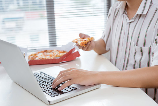 Cropped image of an asian man having lunch with pizza while working at his desk.