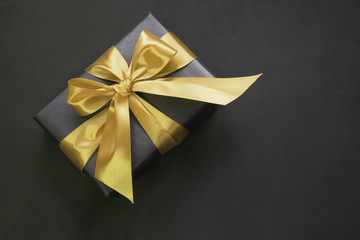 Gift box wrapped in black paper with gold ribbon on black surface.