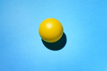 Pallina di gomma di color giallo su fondo blu e ombra di appoggio