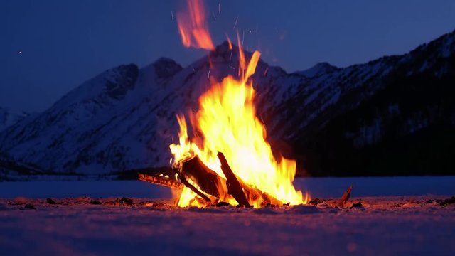 Bonfire on the ice of Lower Multinskoe lake in the Altai Mountains at late evening with snow on mountains