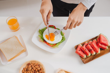 Hands of man cut the eggs on paper, served with bread, herbs, sausage and fresh juice.