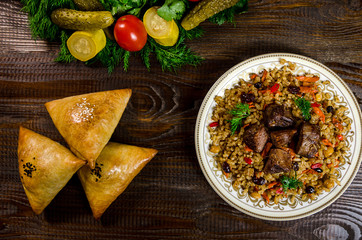 Uzbek national dish of pilaf and samsa on a dark wooden background with pickles