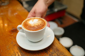 Hand barista holding and serving cup of coffee.