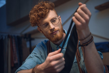 young male fashion designer in eyeglasses holding black necktie