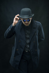 A man in a black cloak and black glasses takes off his hat