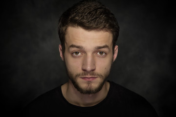 Portrait of a young man with a beard on a dark background.