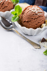 Chocolate ice cream scoop in white bowl with chopped white chocolate and mint decoration. Summer food concept with copy space.