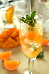 Sparkling cocktail with mango pieces, ice cubes and mint in a wineglass