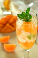 Sparkling cocktail with mango pieces, ice cubes and mint in a wineglass