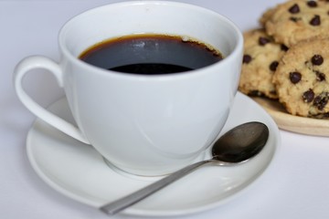 A coffee cup with chocolate chip cookies on the wooden dish on white background