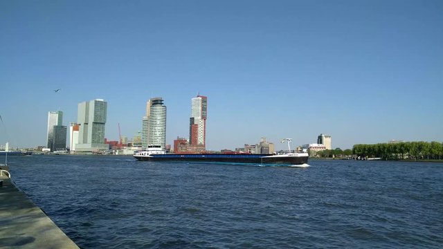 ROTTERDAM skyline Kop van Zuid district, built on abandoned port areas, with historic and modern architecture. Inland ship navigates downstream Nieuwe Maas waterway. THE NETHERLANDS - MAY 2016
