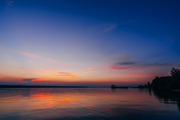 sunset over water of river with a pier and a beach with beautiful red and blue sky