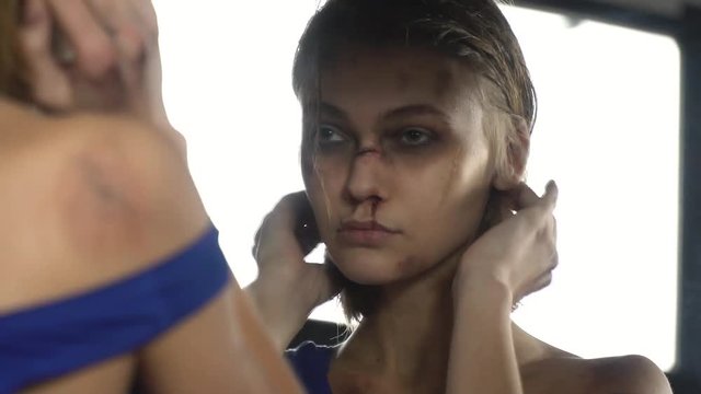 A girl looks in the mirror at her bruises and scars