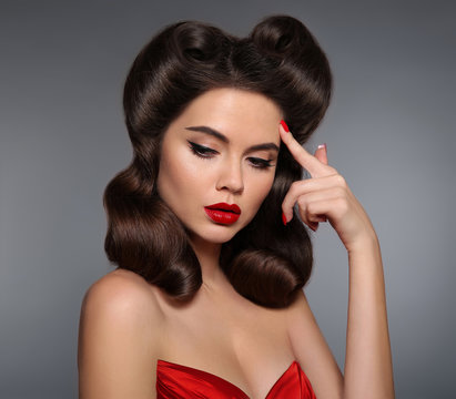 Nostalgia. Pin up girl with red lips makeup and retro curls hair style. Retro woman looking to the side holds a finger near the head. Expressive facial expressions. High fashion photo.