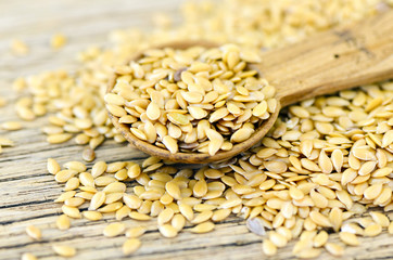 Spoonful of golden flax seed on wood background.