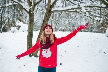Fototapeta na wymiar Blonde girl in red scarf, hat and santas sweater posing at park on winter day.