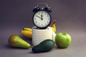Alarm clock, fruits and toilet paper on a dark background. Natural remedy for constipation