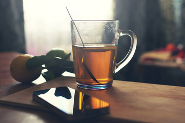 smartphone with cup of tea and lemon on wooden board