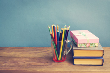 Color pencils, books and gift box on wooden background.