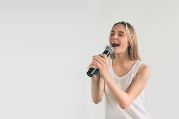 Girl Rocking Out. Image of a women singing to the microphone, isolated on light. Emotional portrait of an attractive kid on a gray background.