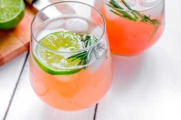 sliced lime, rosemary and natural juice in glass on white table 