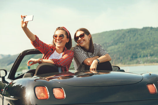 Two female freinds take a selfie photo in cabriolrt car during their summer voyage