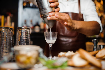 Bartender in a brown leather apron pouring cocktail into the glass