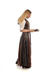 Fototapeta premium full length portrait of girl wearing brown fantasy costume, holding a book. standing pose on white studio background. 