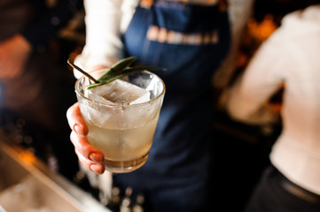 Waitress dressed in a white shirt and blue apron holding a glass with cold drink