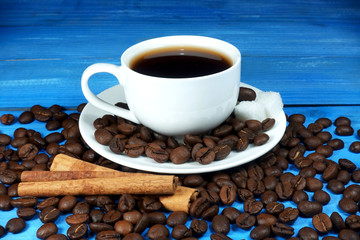 White cup of coffee with a bunch of coffee beans and cinnamon sticks on blue wooden table