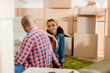 dreamy african american couple in new apartment with cardboard boxes