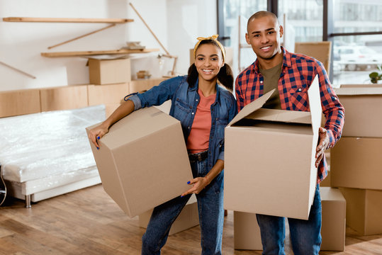 happy african american couple holding cardboard boxes and moving to new home