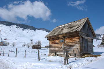 Wooden barn in the winter/Winter image with an old village wooden barn in the foreground and snowy hills in the background.