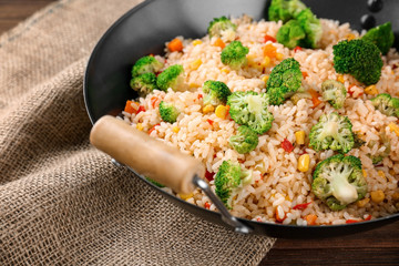 Delicious rice pilaf with broccoli in wok on wooden table