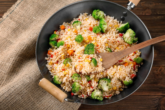 Delicious rice pilaf with broccoli in wok on wooden table