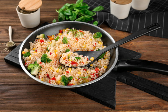 Delicious rice pilaf with broccoli in frying pan on wooden table