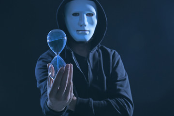 Masked hacker with sand clock in darkness