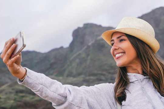 Young beautiful woman in vacation taking a selfie with her mobile smartphone camera with mountain in the background - Phone, social, addiction and travel concept