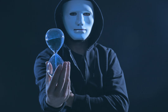 Masked hacker with sand clock in darkness