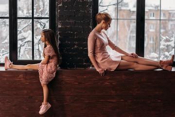 depressed mother and daughter sitting on windowsills back to back