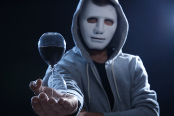 Masked hacker with sand clock in darkness