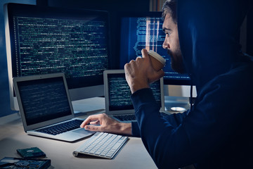 Man drinking coffee while hacking server in dark room