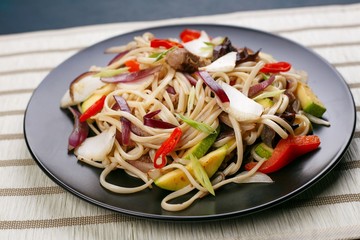 Udon wok noodles with pork and peppers, served on black plate, close up. Japanese cuisine, restaurant concept