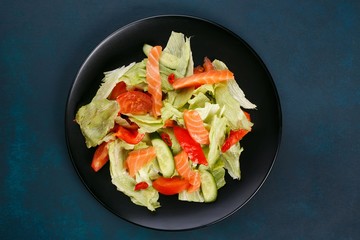 Freshly made vegetable salad with salmon on black plate, healthy diet food, flat lay