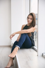 Depressed young woman after breakup sitting on window sill indoors