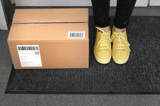 Woman standing near delivered parcel on doormat, closeup