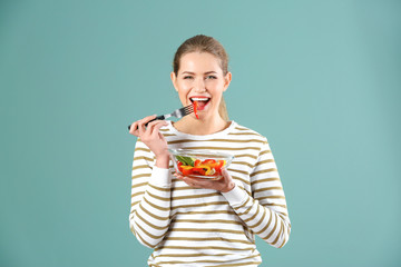 Young beautiful woman eating fresh salad on color background