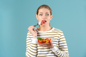 Young beautiful woman eating fresh salad on color background
