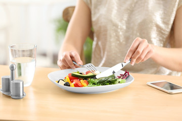 Obraz na płótnie Canvas Young woman eating fresh salad at table
